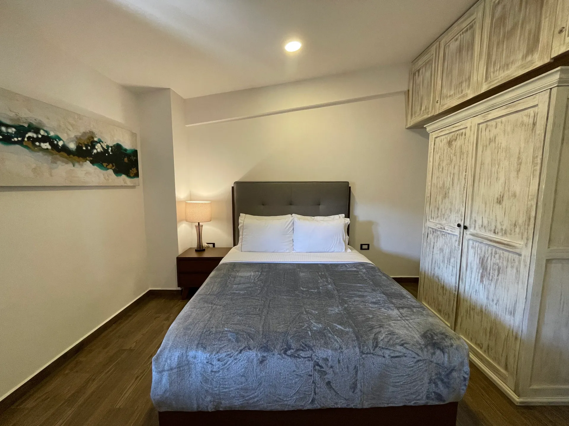 Bedroom with gray bedspread, artwork, and white armoire.