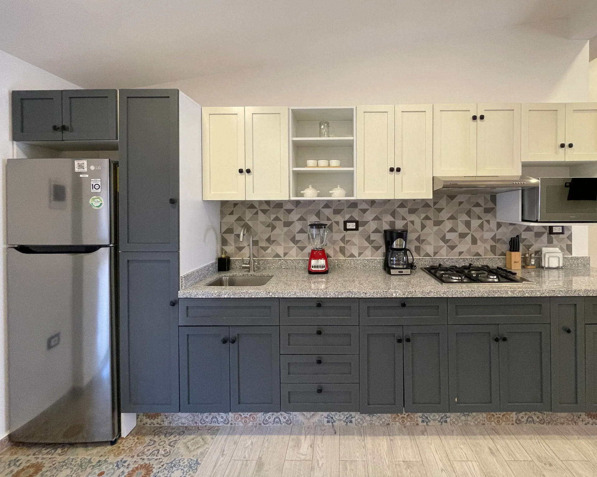 Cocina con gabinetes grises y blancos, refrigerador de acero inoxidable y encimera con electrodomésticos.