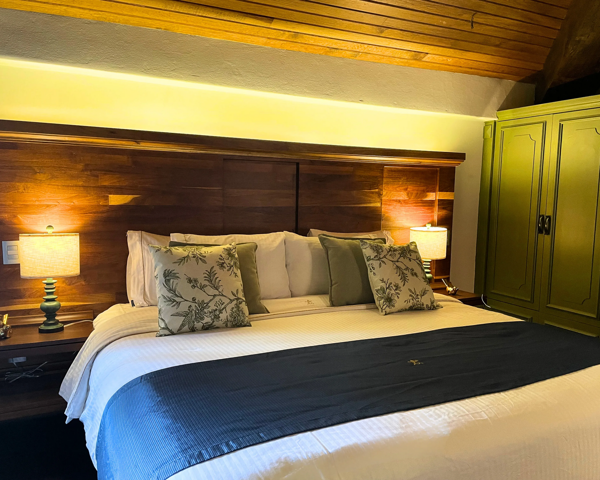 Acogedor dormitorio con una cama grande, mesitas de noche, lámparas y un armario verde. Iluminación cálida .