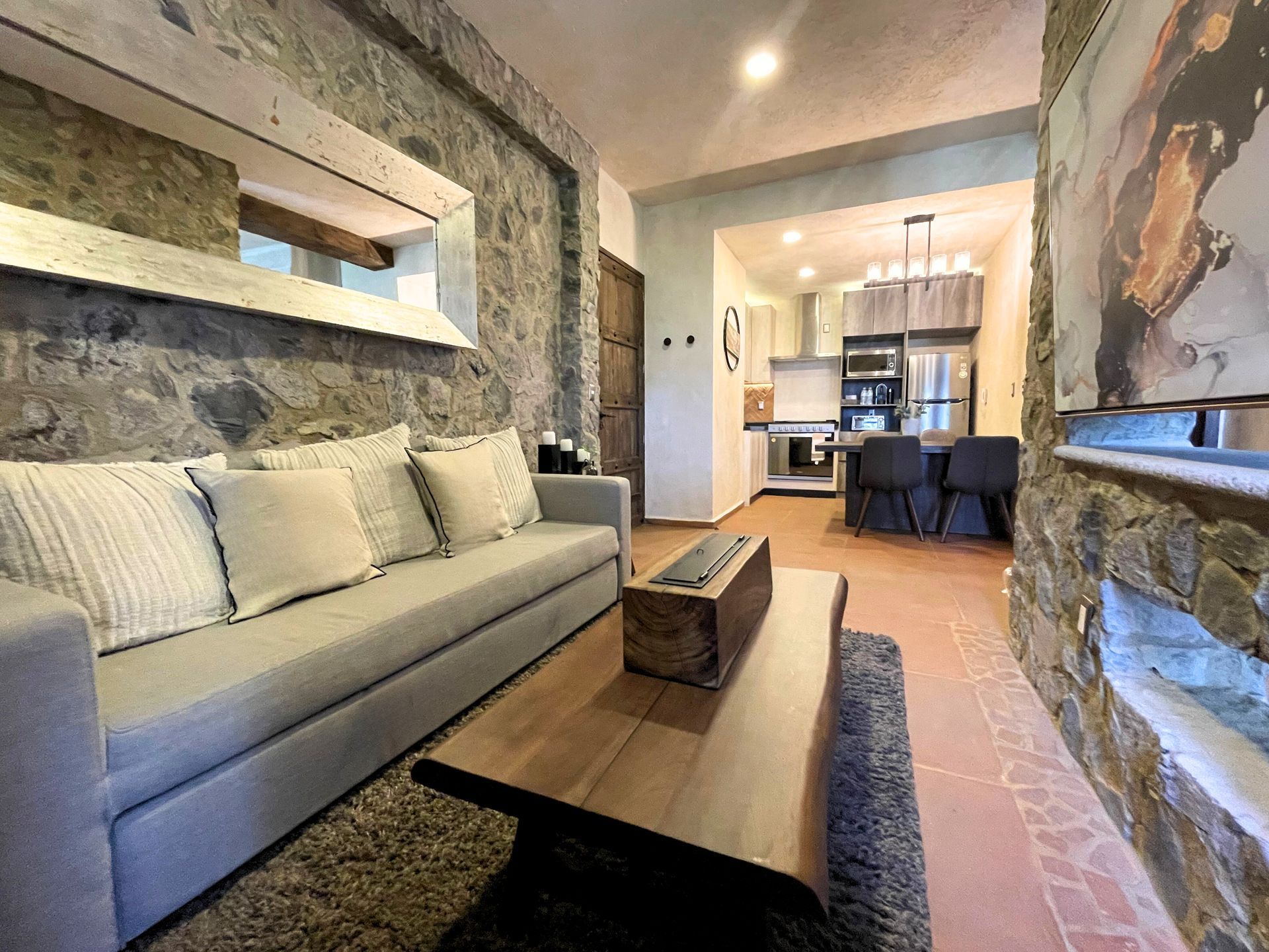 Modern living room with a beige sofa, coffee table, textured stone wall, and open dining area beyond