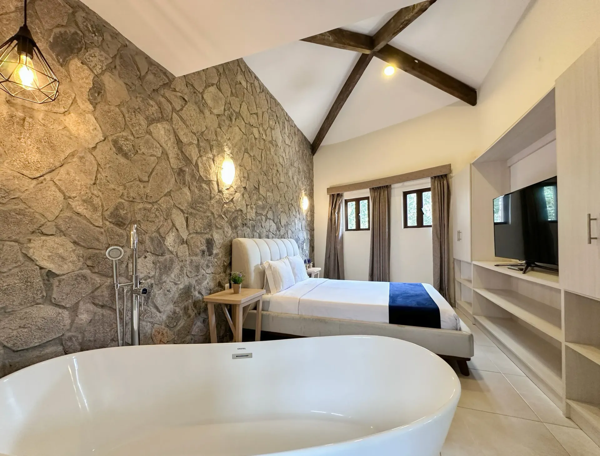 Bedroom with stone accent wall, tub, bed, TV, and open shelves.