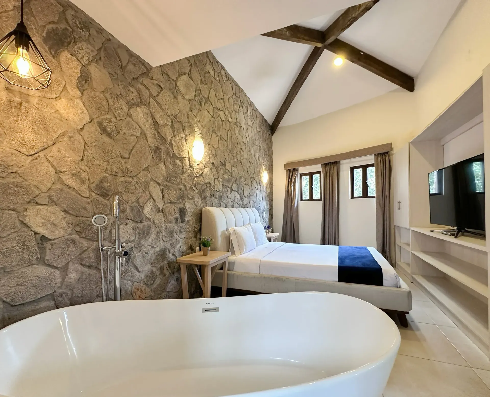 A bedroom with a stone wall, bed, and freestanding bathtub.