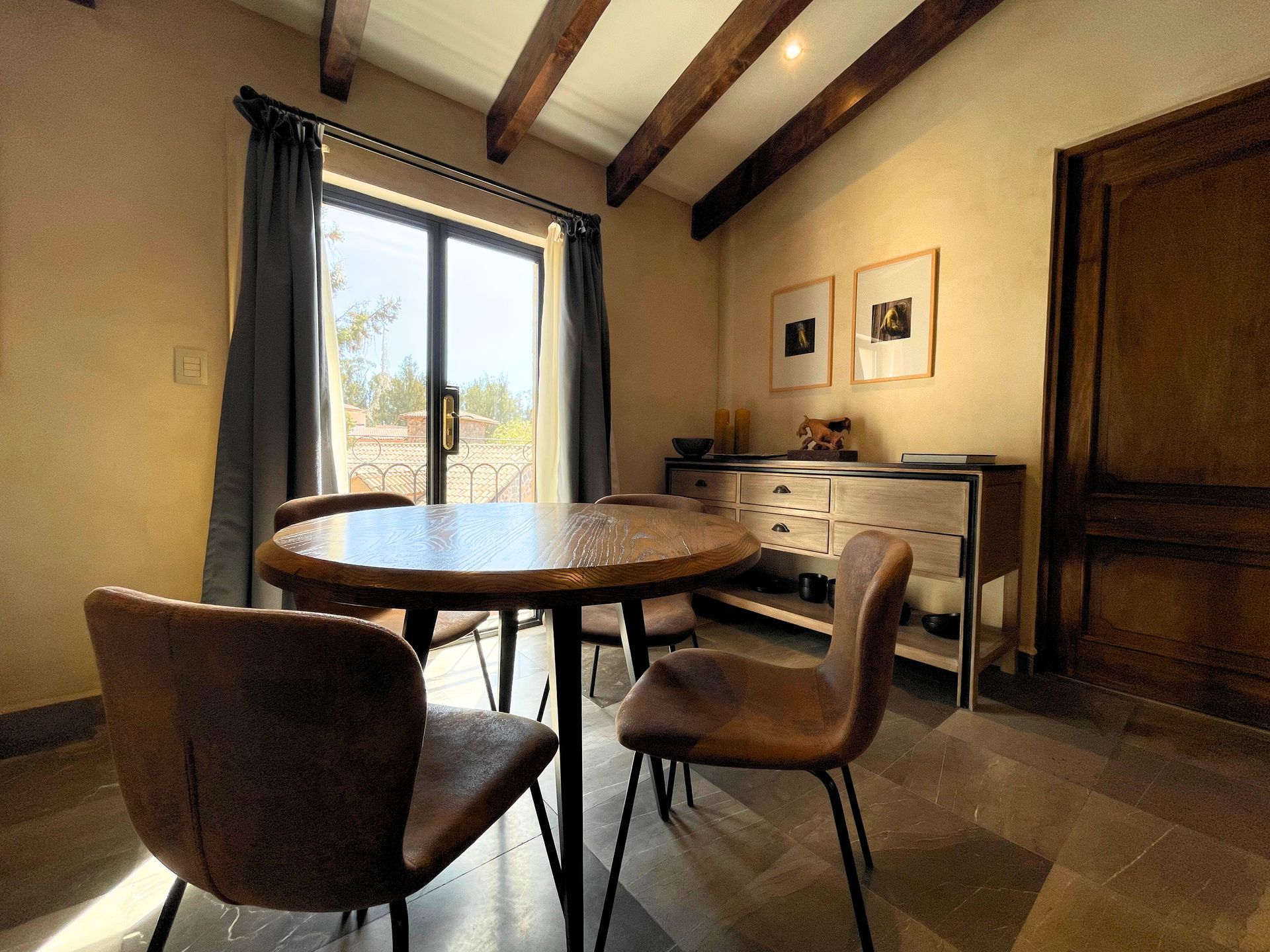 Cozy dining room with round table, two chairs, sideboard, and open patio doors to sunlight