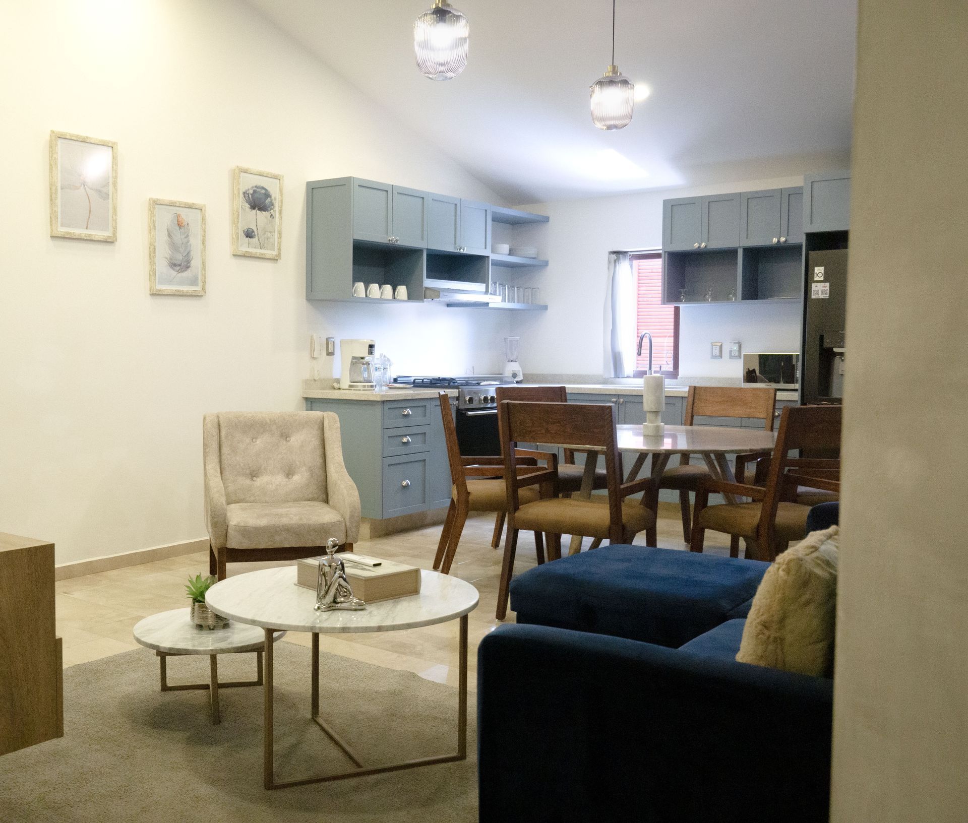 Cozy living room with blue sofa and chairs opening to a small blue kitchen and dining area.