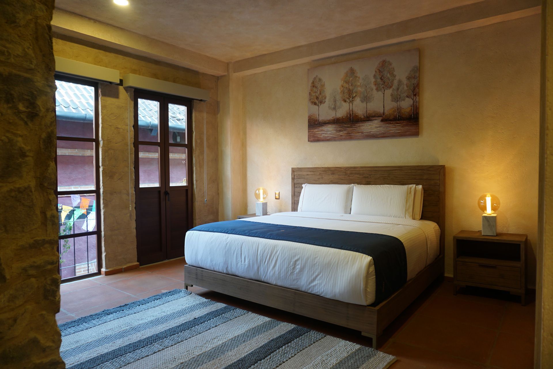 Cozy hotel bedroom with king bed, bedside lamps, rug, and balcony doors with warm lighting