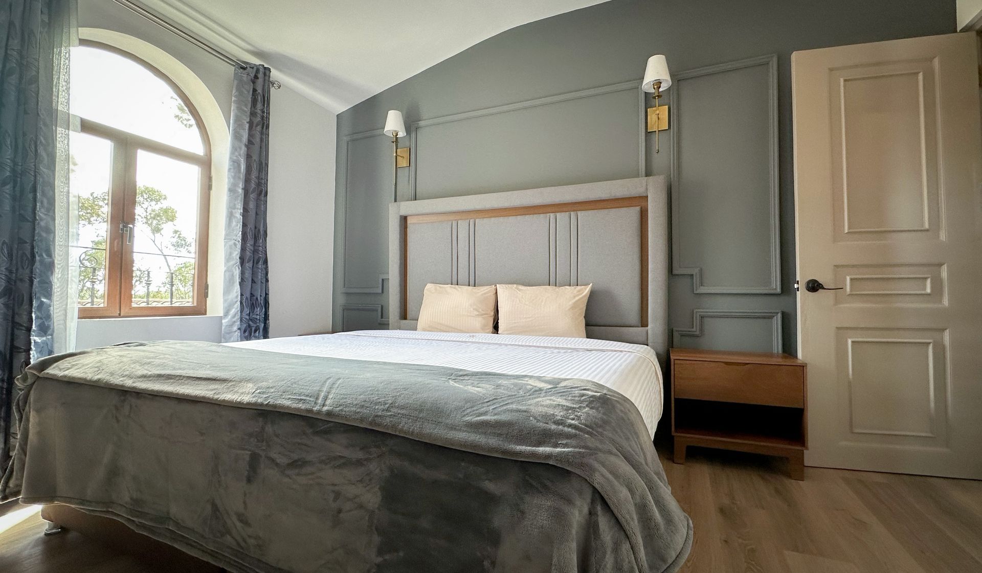 Dormitorio con cama, ventana y paredes grises. La luz del sol entra a raudales por la ventana.