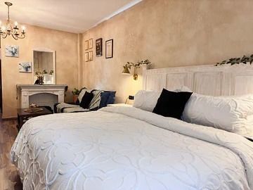 Acogedor dormitorio con gran cama blanca, sofá, chimenea y paredes en tonos neutros.