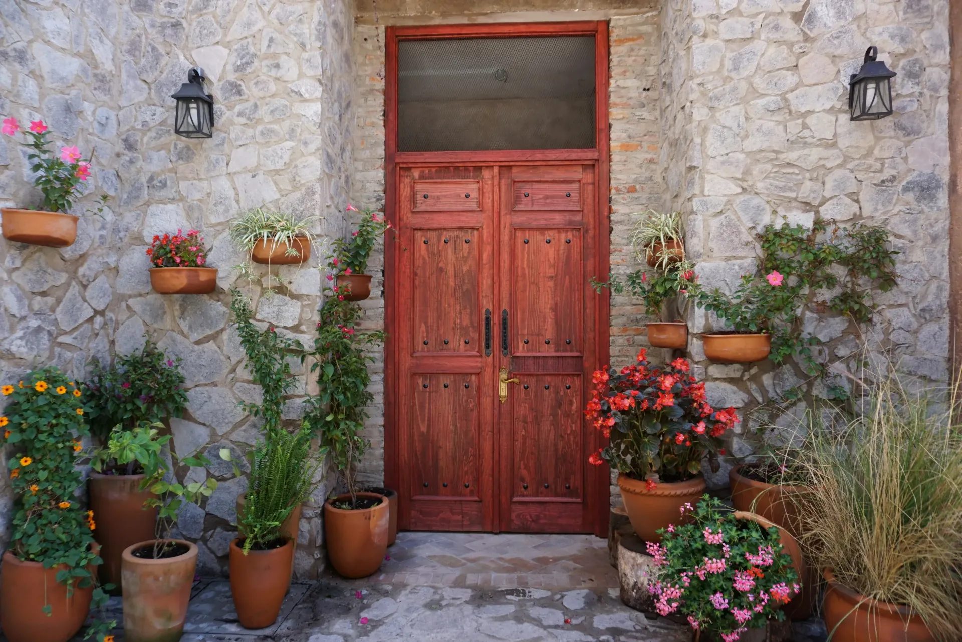 Puerta de madera roja enmarcada por paredes de piedra y plantas en macetas.