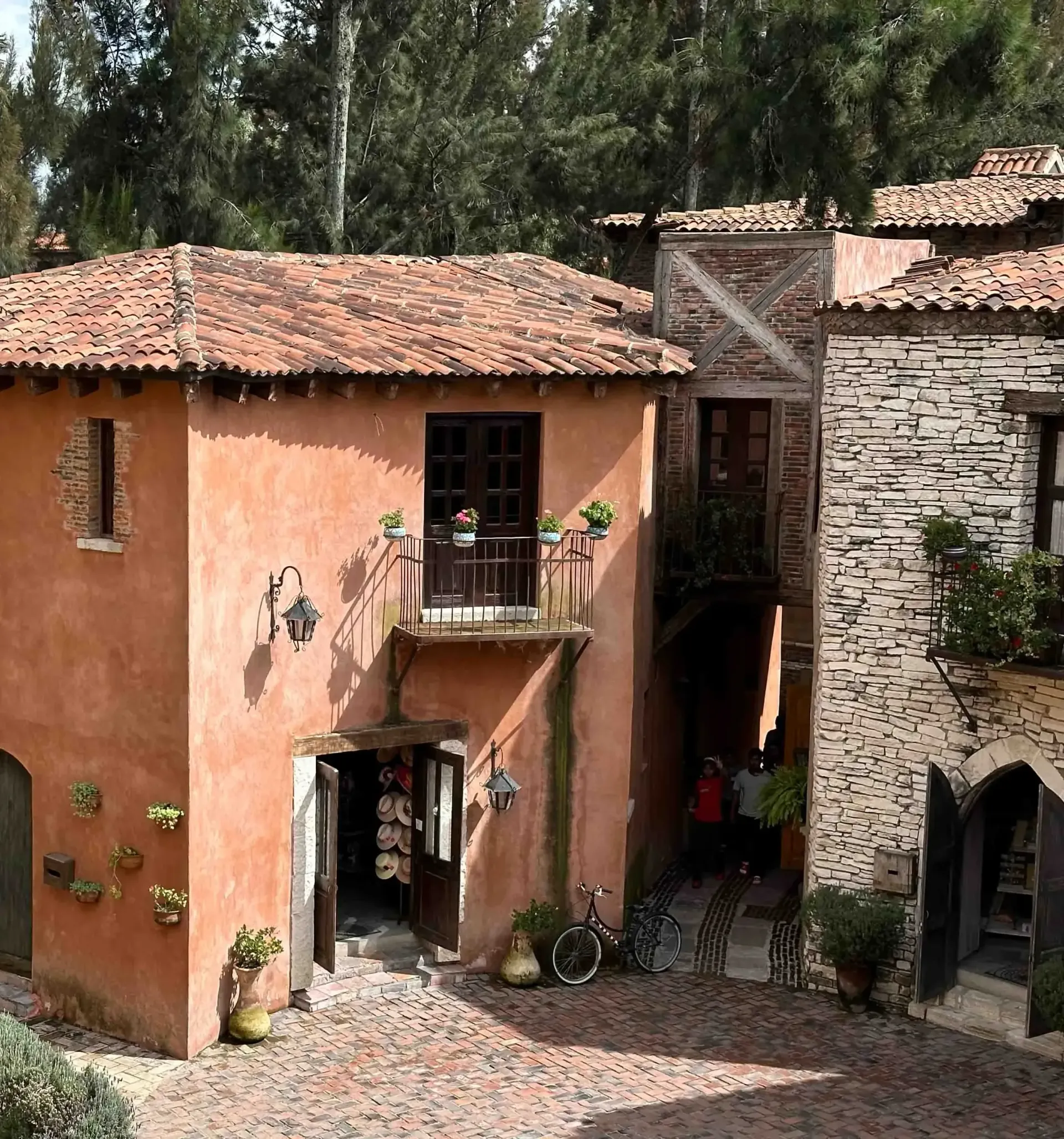 Stone buildings with terracotta roofs, cobblestone pathway. Entrance to building is open.