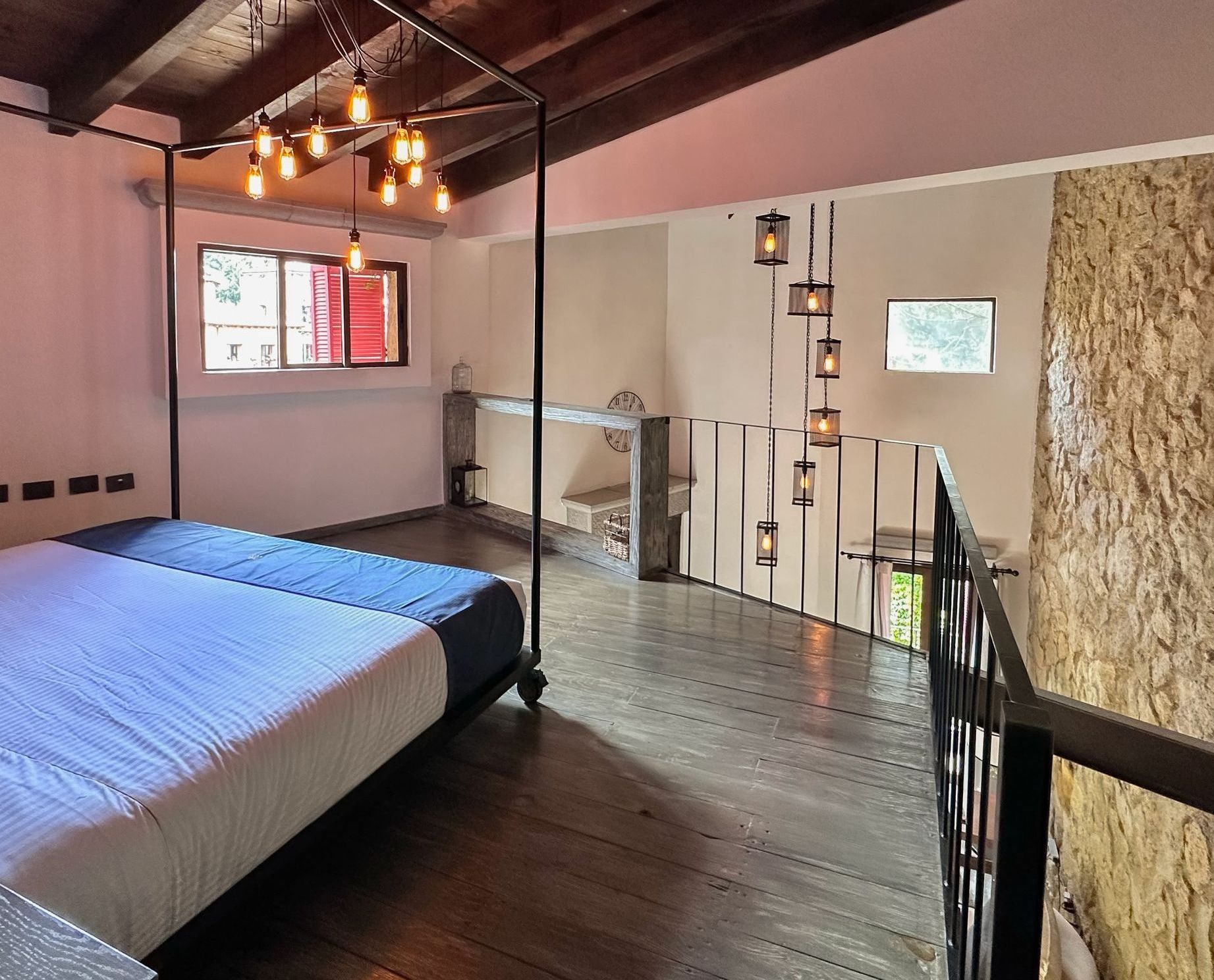 Bedroom with a four-poster bed, exposed beams, and a loft with hanging lights.