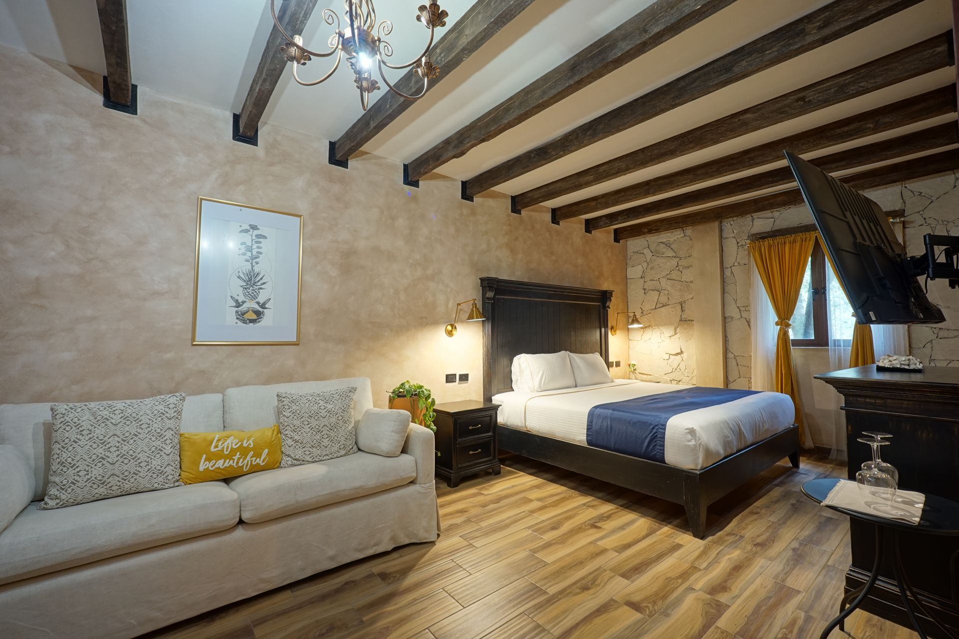 Cozy rustic bedroom with exposed beams, a bed, sofa, and warm neutral decor