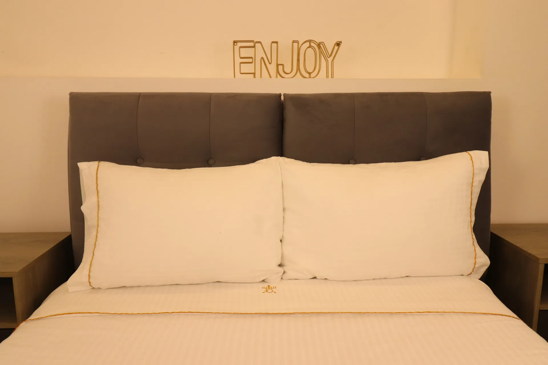 Dormitorio con ropa de cama blanca, dos almohadas, cabecera gris y cartel