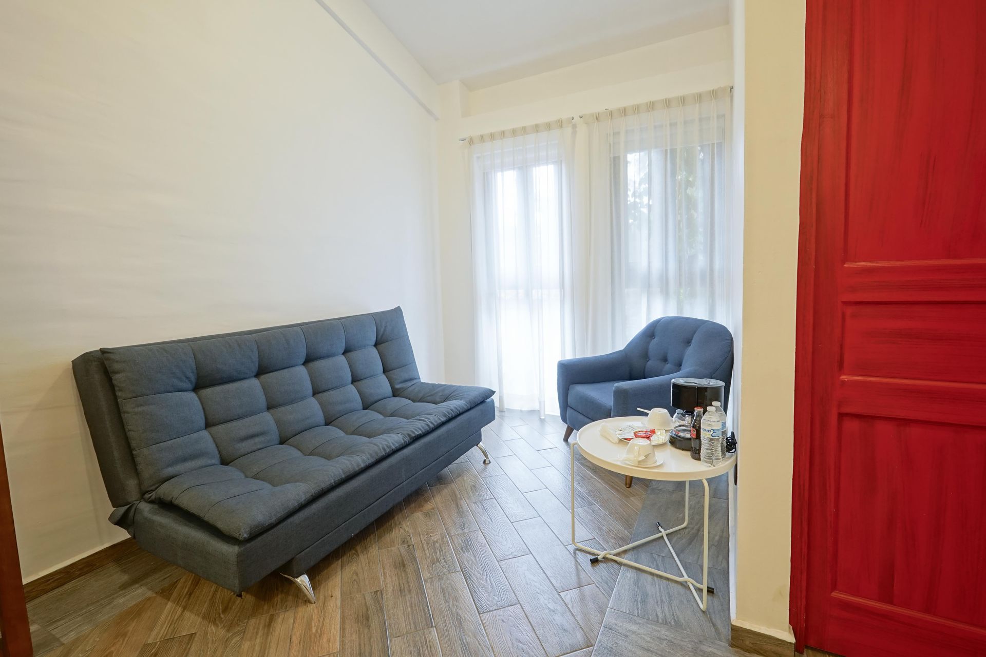 Bright living room with blue sofa, armchair, small white table, and red cabinet by a window