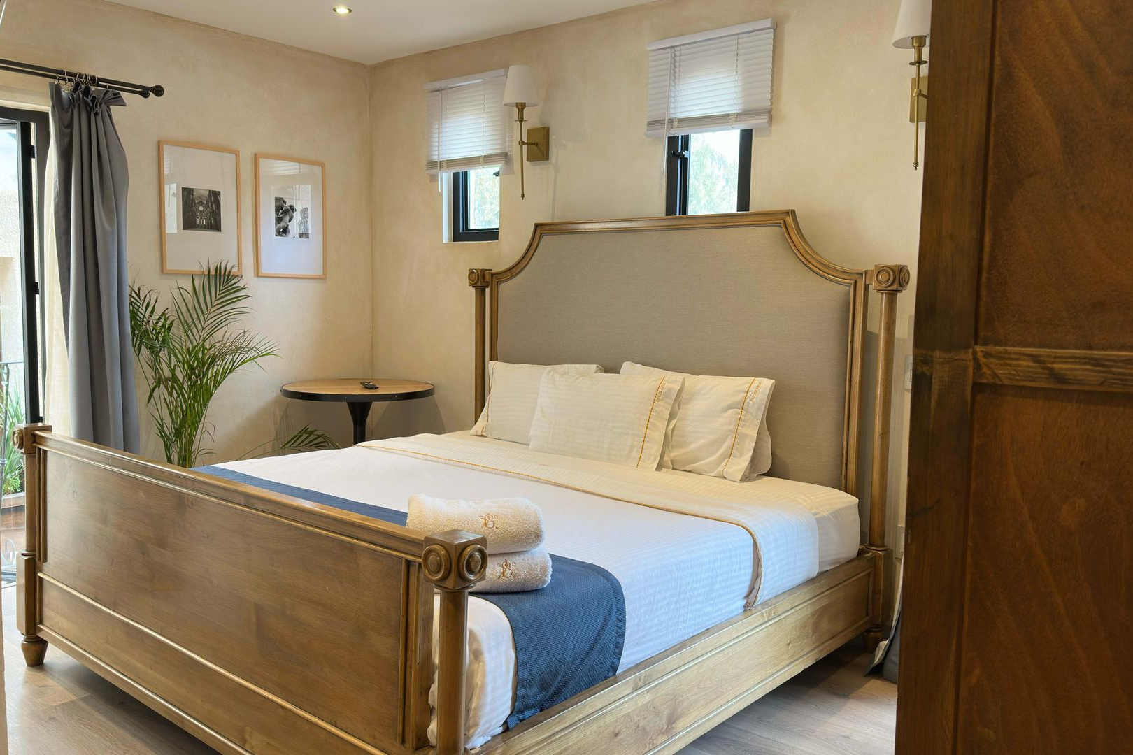 Bed with a gray upholstered headboard, white pillows, and gold wall sconces on a beige wall.