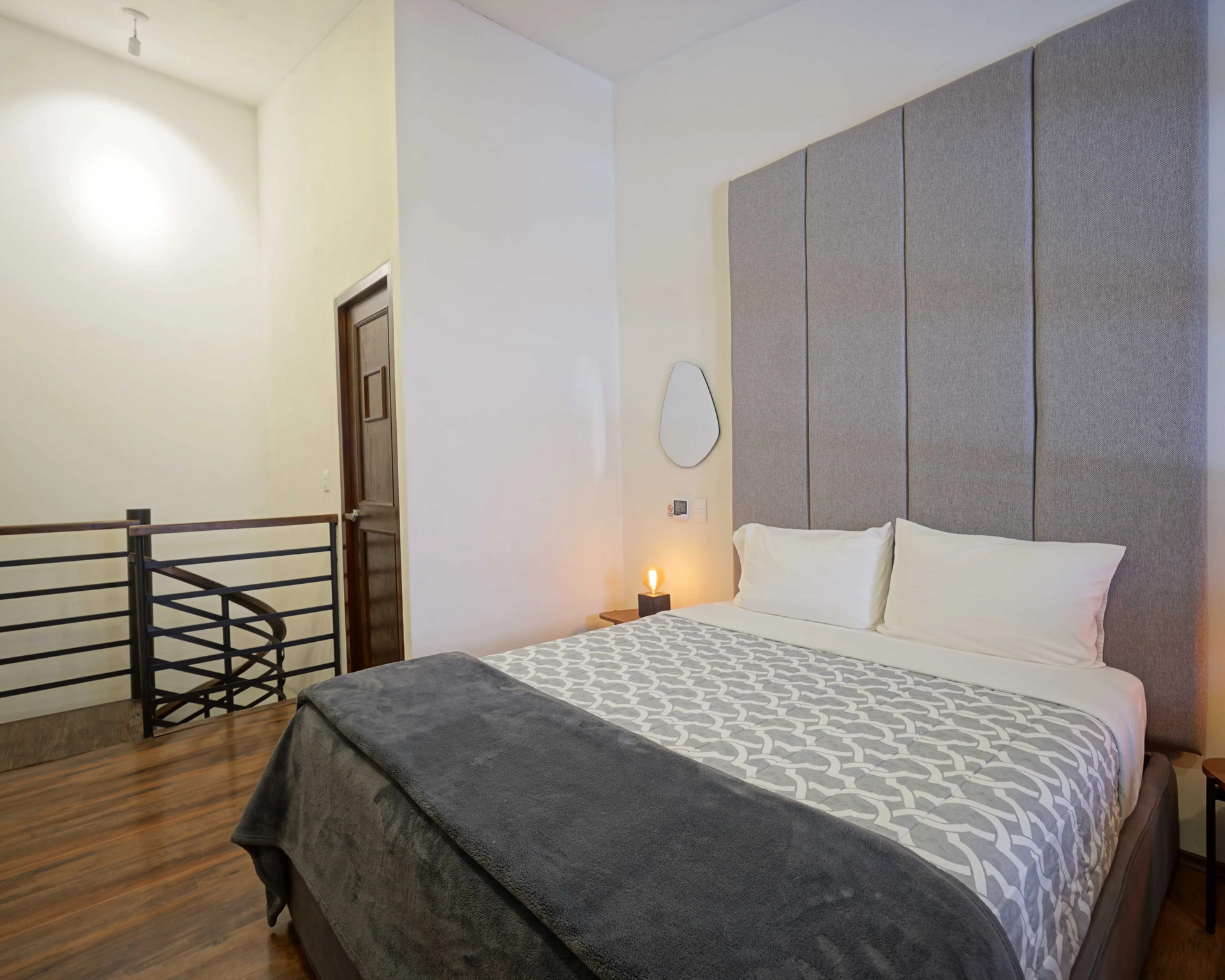 Bedroom with gray upholstered headboard, bed, and spiral staircase leading up.