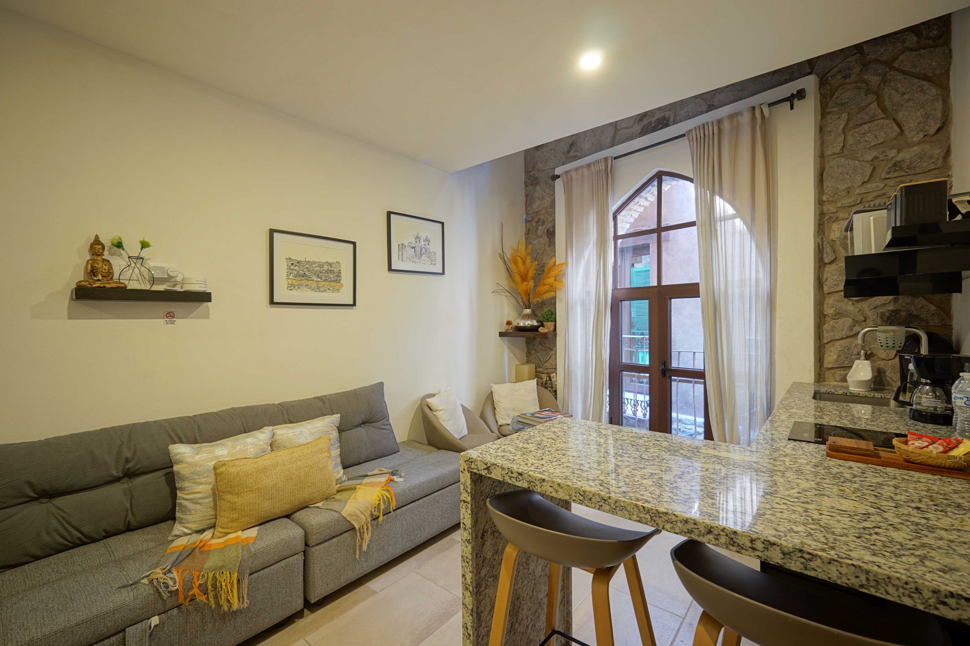 Cozy living room with gray sofa, patterned rug, dining table, and large arched window by a stone fireplace
