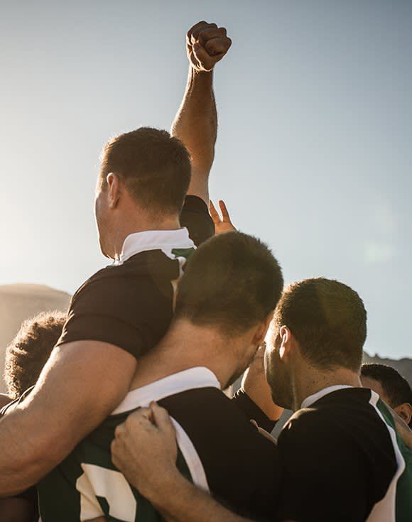 A group of rugby players are huddled together and one of them has his fist in the air.