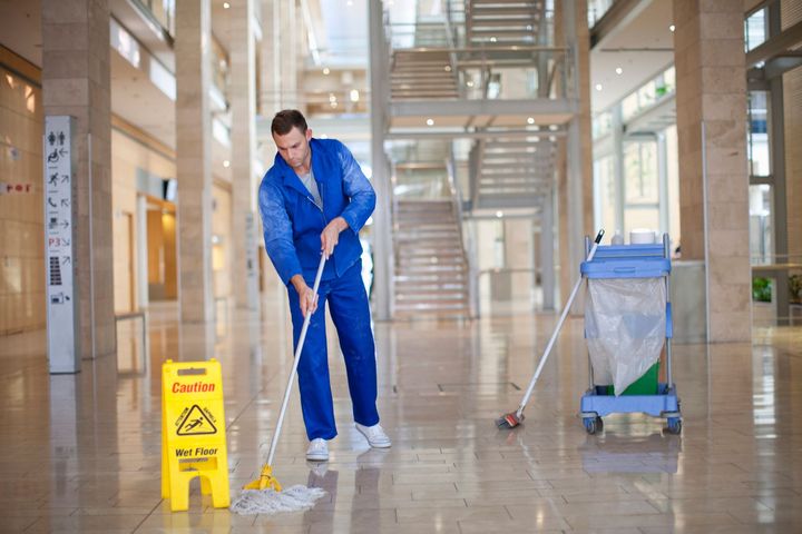 A man is mopping the floor of a building next to a caution sign.