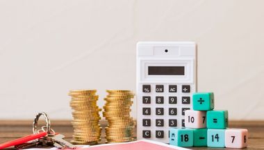 A calculator , stacks of coins , keys and blocks on a wooden table.