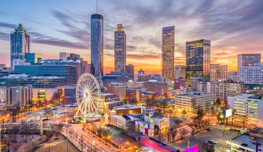 An aerial view of Atlanta city skyline at sunset with a Ferris wheel in the foreground.