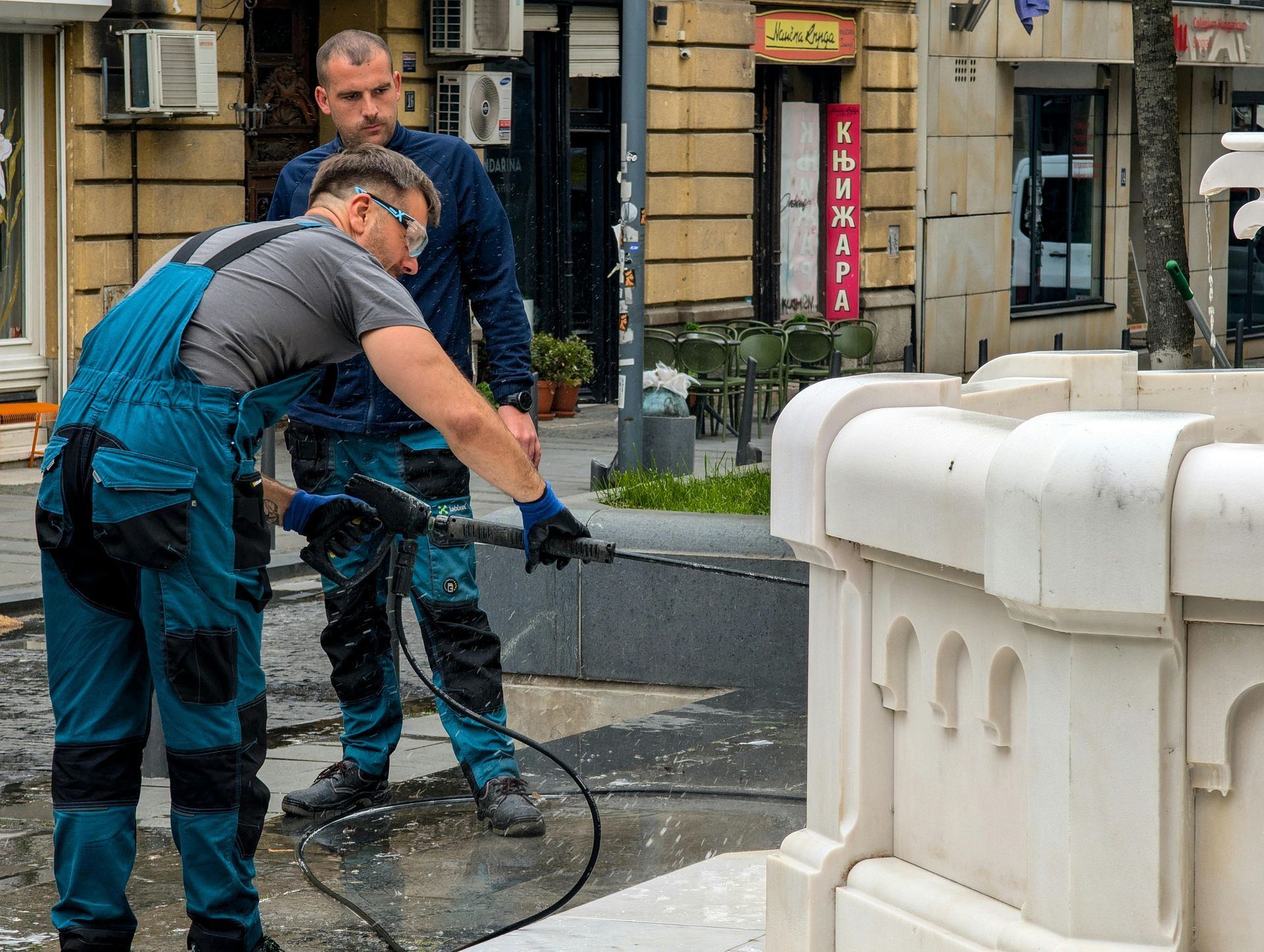 Two men are cleaning a fountain with a high pressure hose.
