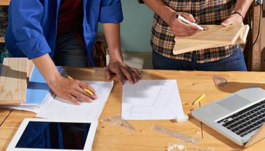 Two men are working on a wooden table with a laptop and a tablet.