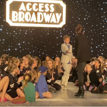 A group of children are gathered in front of a sign that says access broadway