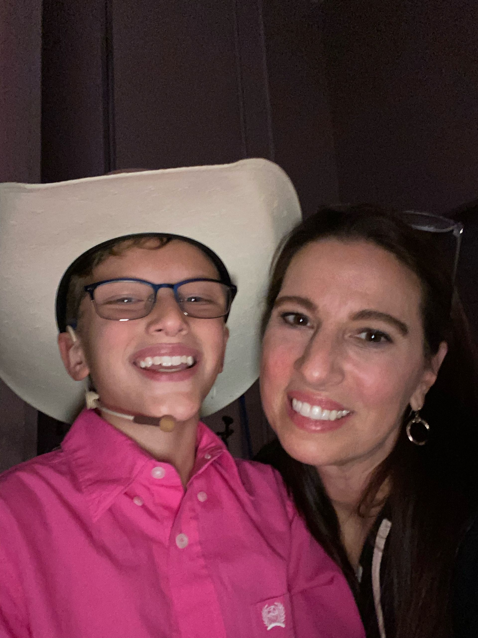 A woman and a boy are posing for a picture . the boy is wearing a cowboy hat and glasses.