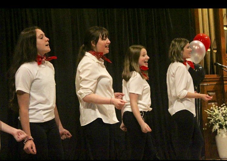 A group of girls singing on a stage with balloons in the background