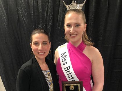 A woman is standing next to a woman wearing a sash that says miss bristol.