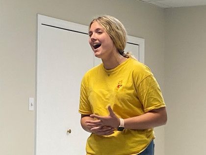 A woman in a yellow shirt is standing in front of a door.