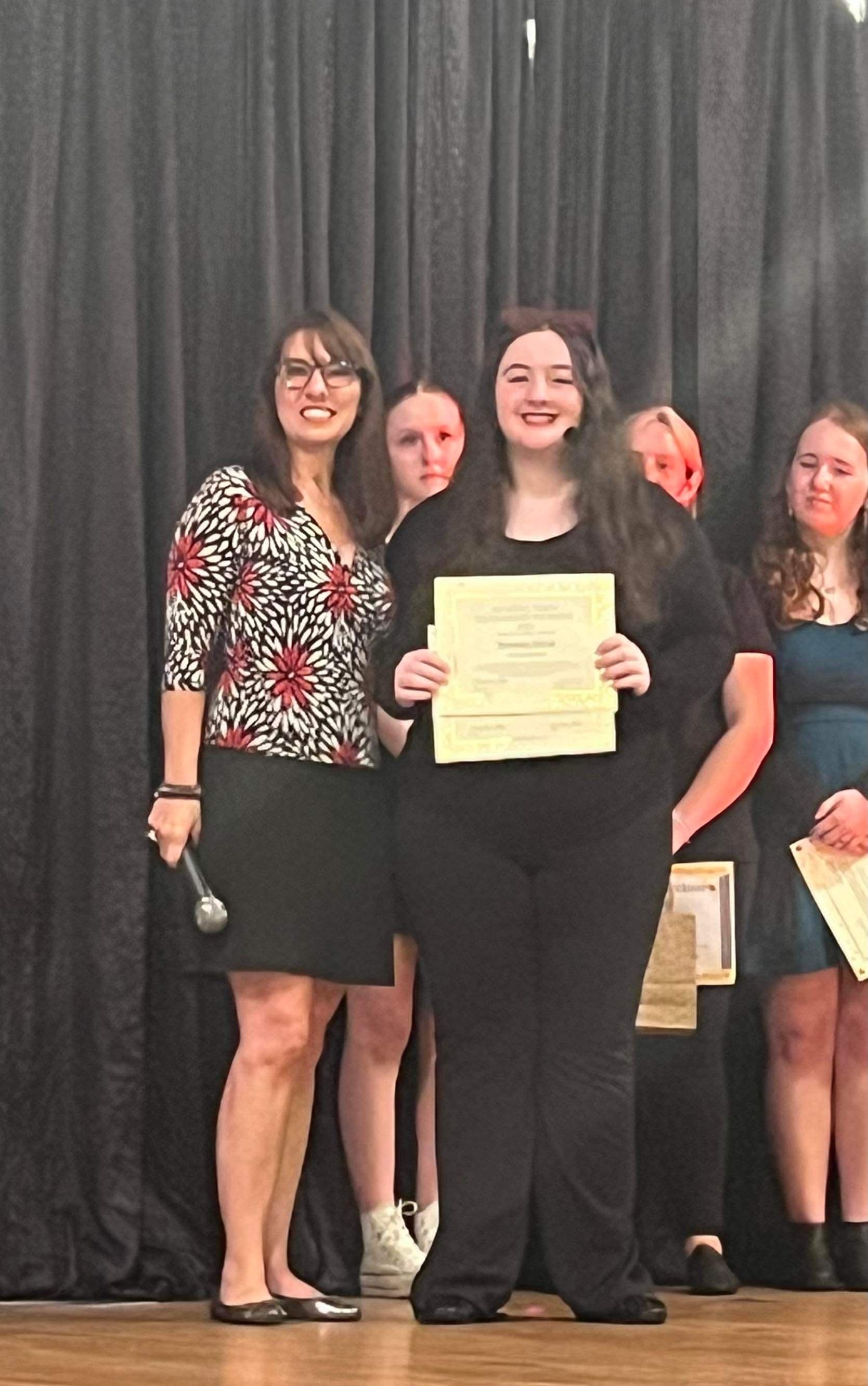 Two women are standing next to each other on a stage holding a certificate.