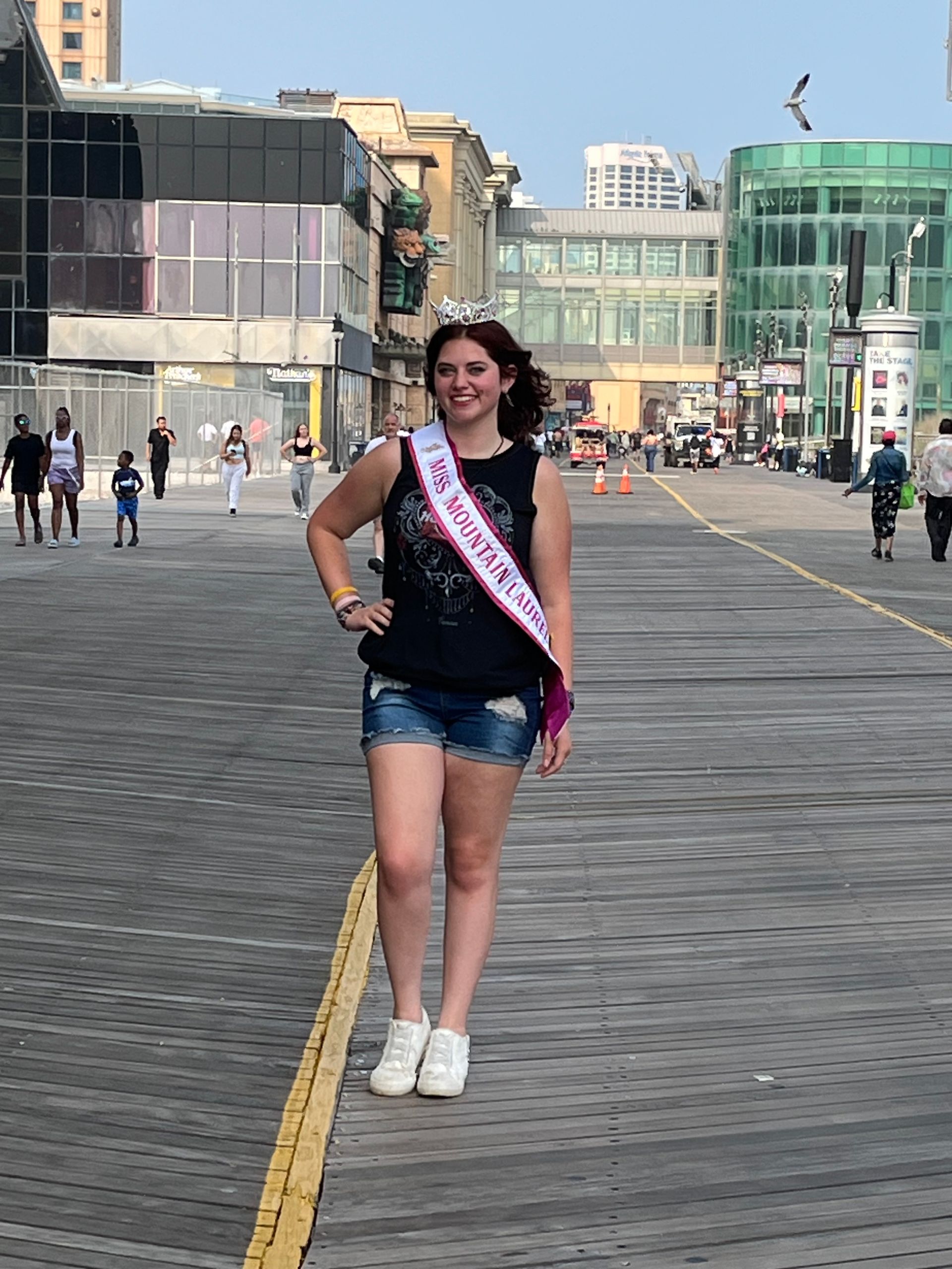 A woman is standing on a boardwalk wearing a sash that says bachelorette.