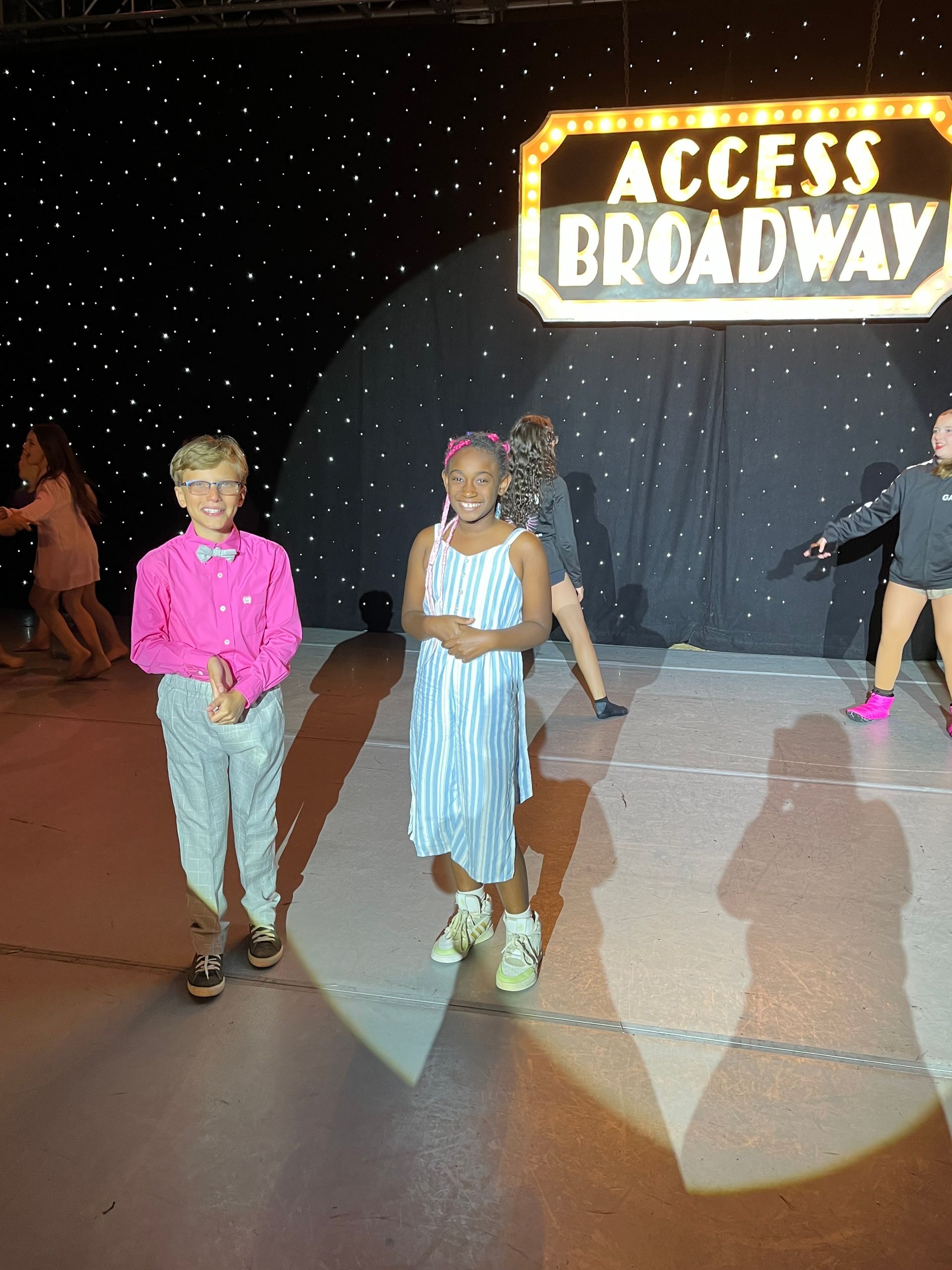 A group of children are standing on a stage in front of a sign that says access broadway