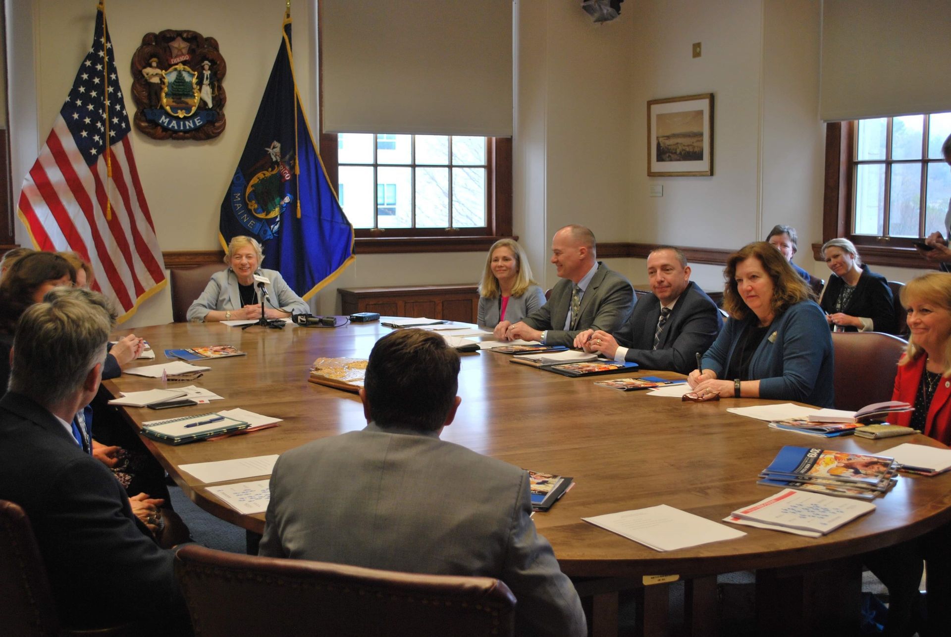 A group of people are sitting around a table with flags in the background.