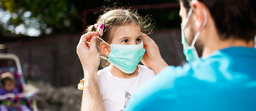 A man is putting a face mask on a little girl.
