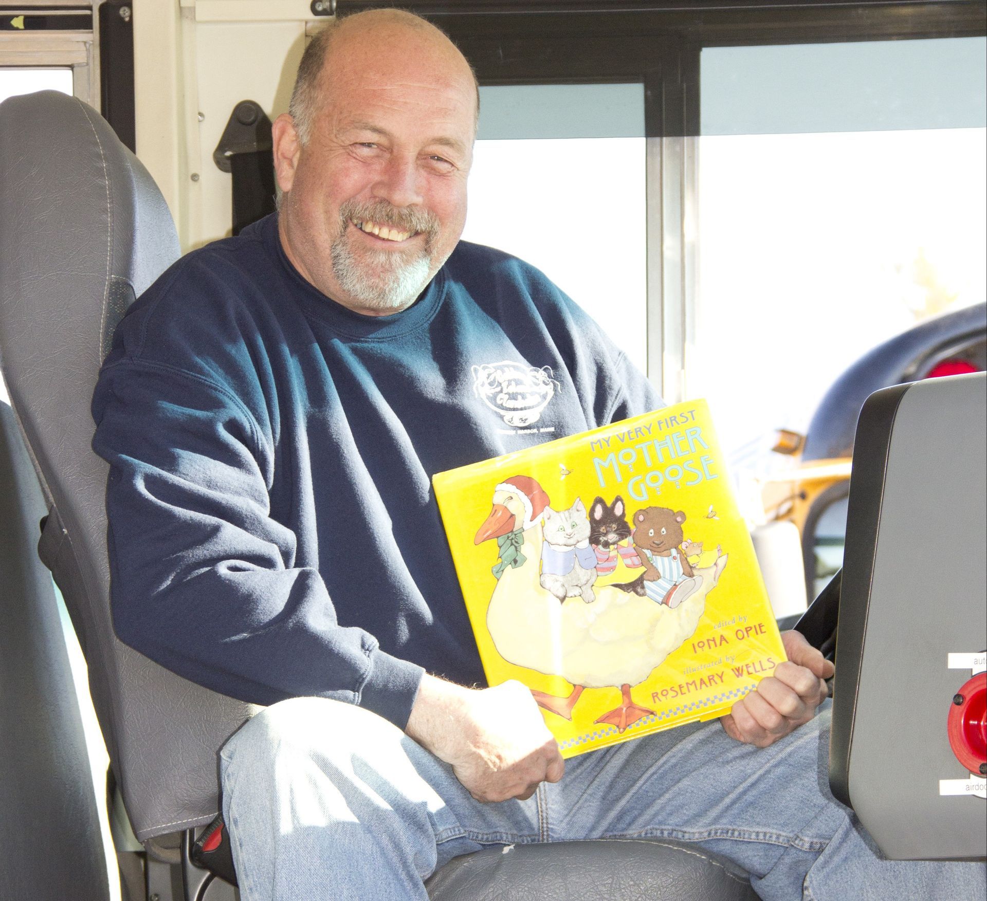 A man is sitting on a bus holding a book about a duck