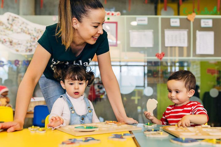 A woman is playing with two children in a classroom.