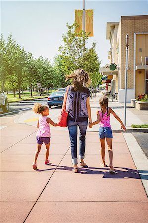 A woman and two little girls are walking down a sidewalk holding hands.
