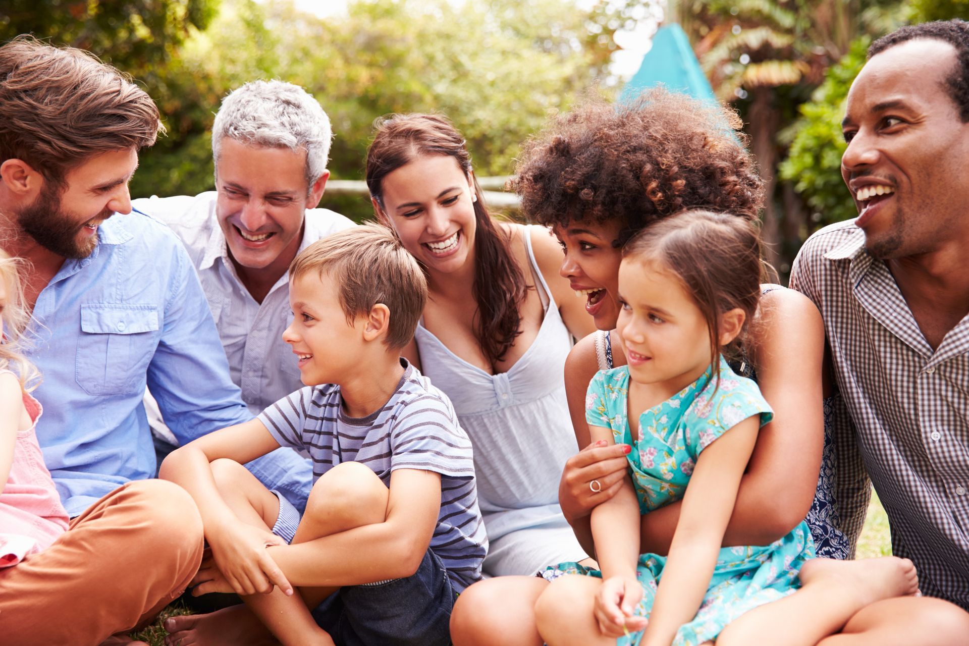 A large family is sitting on the ground in a park.