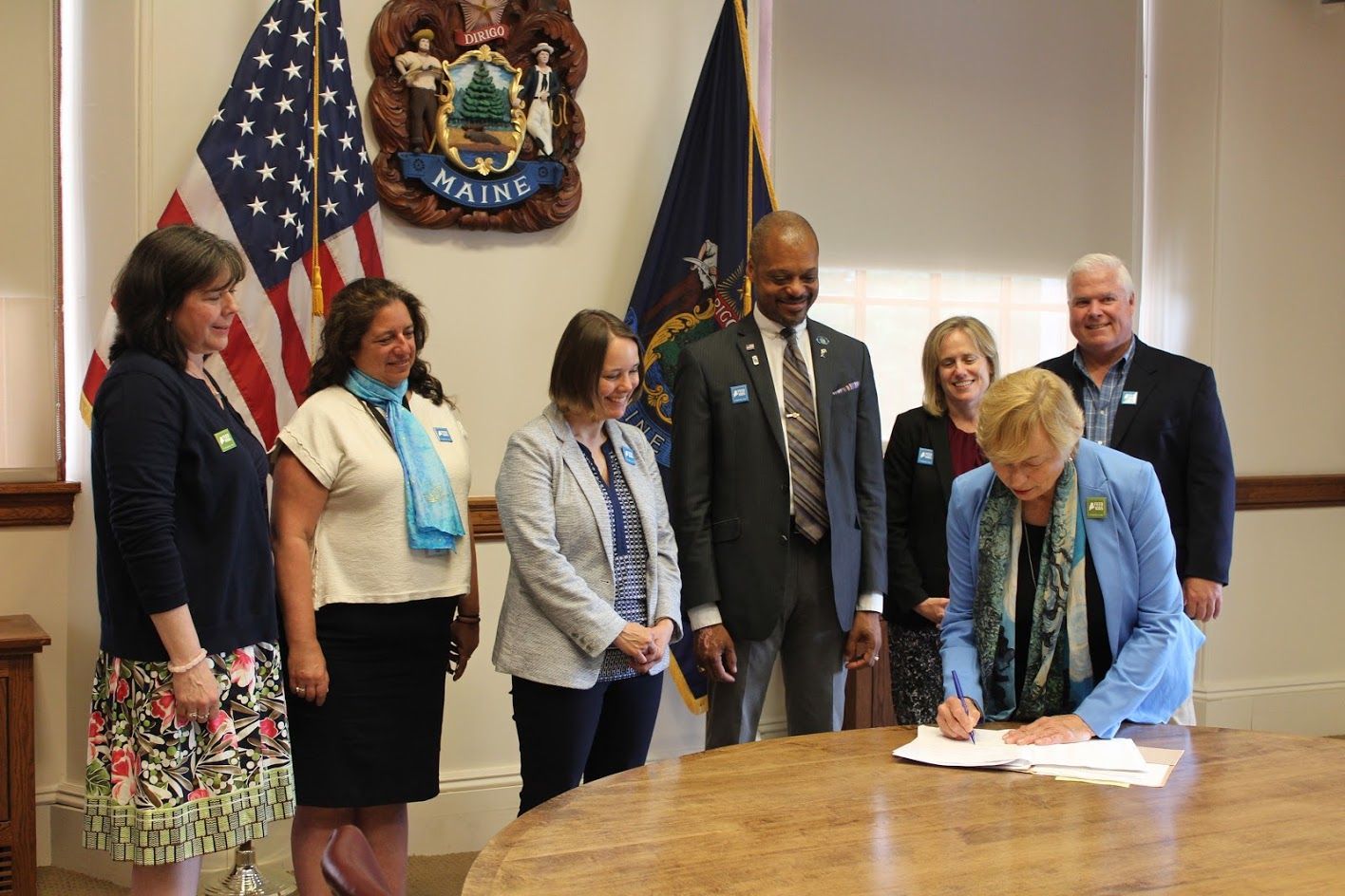 A group of people are standing around a table with a woman signing a document.