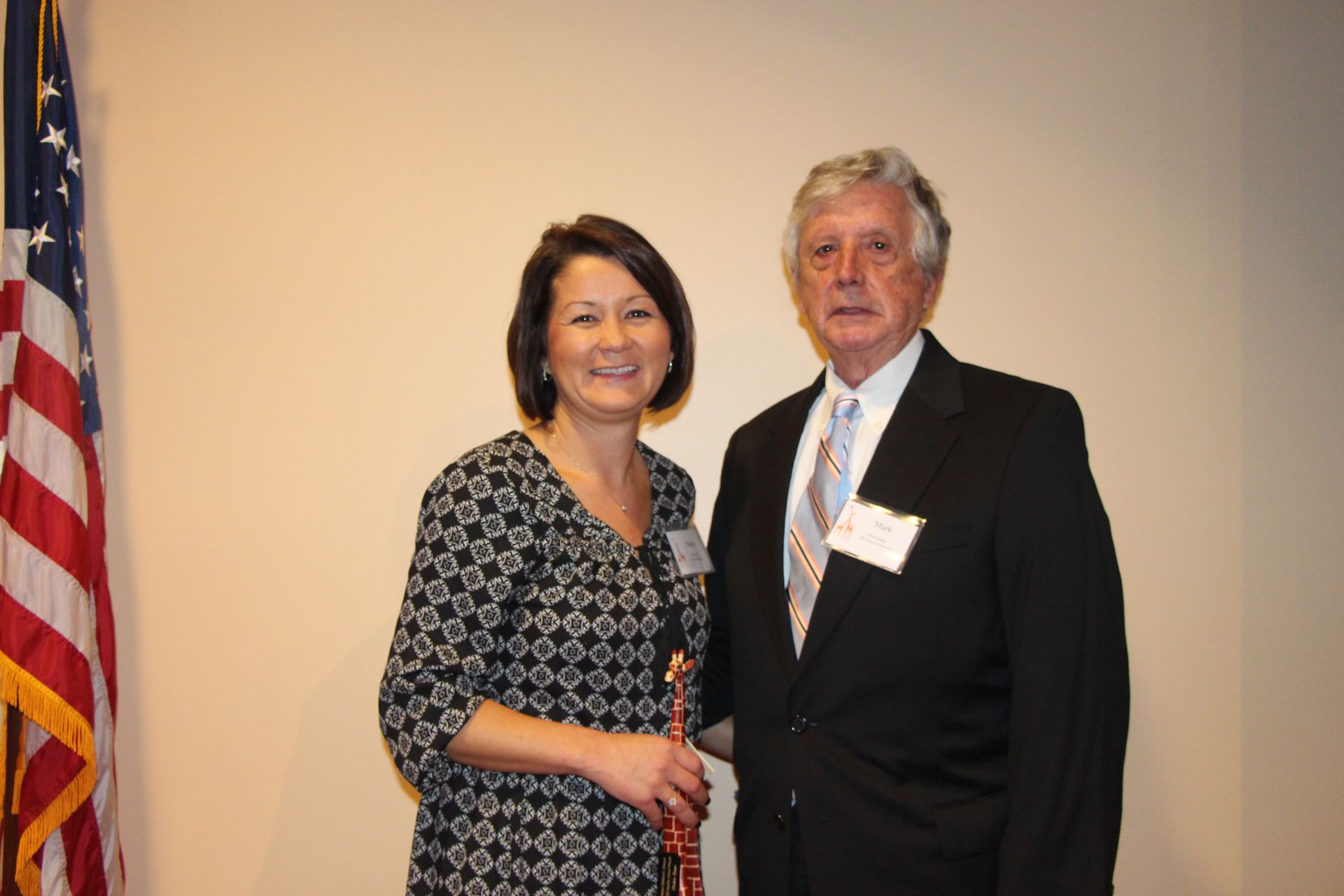 A man and a woman are posing for a picture in front of an american flag.