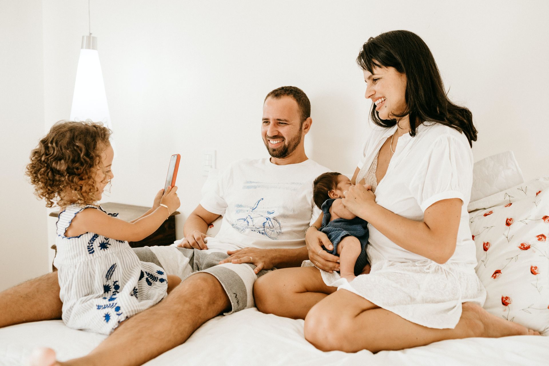 A family is sitting on a bed with a baby and a little girl.