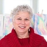 A woman in a red sweater is smiling in front of a painting.