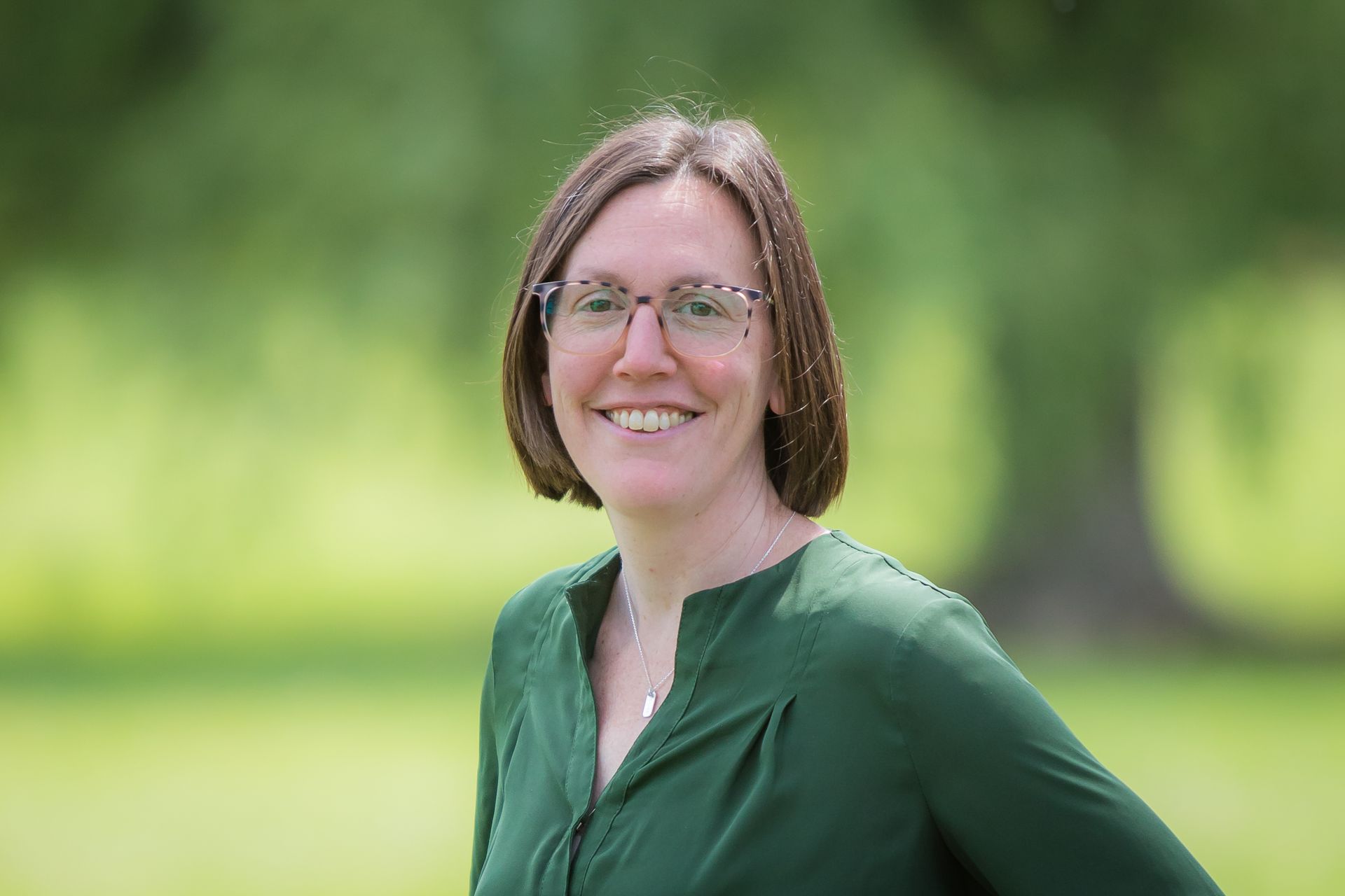 A woman wearing glasses and a green shirt is smiling for the camera.