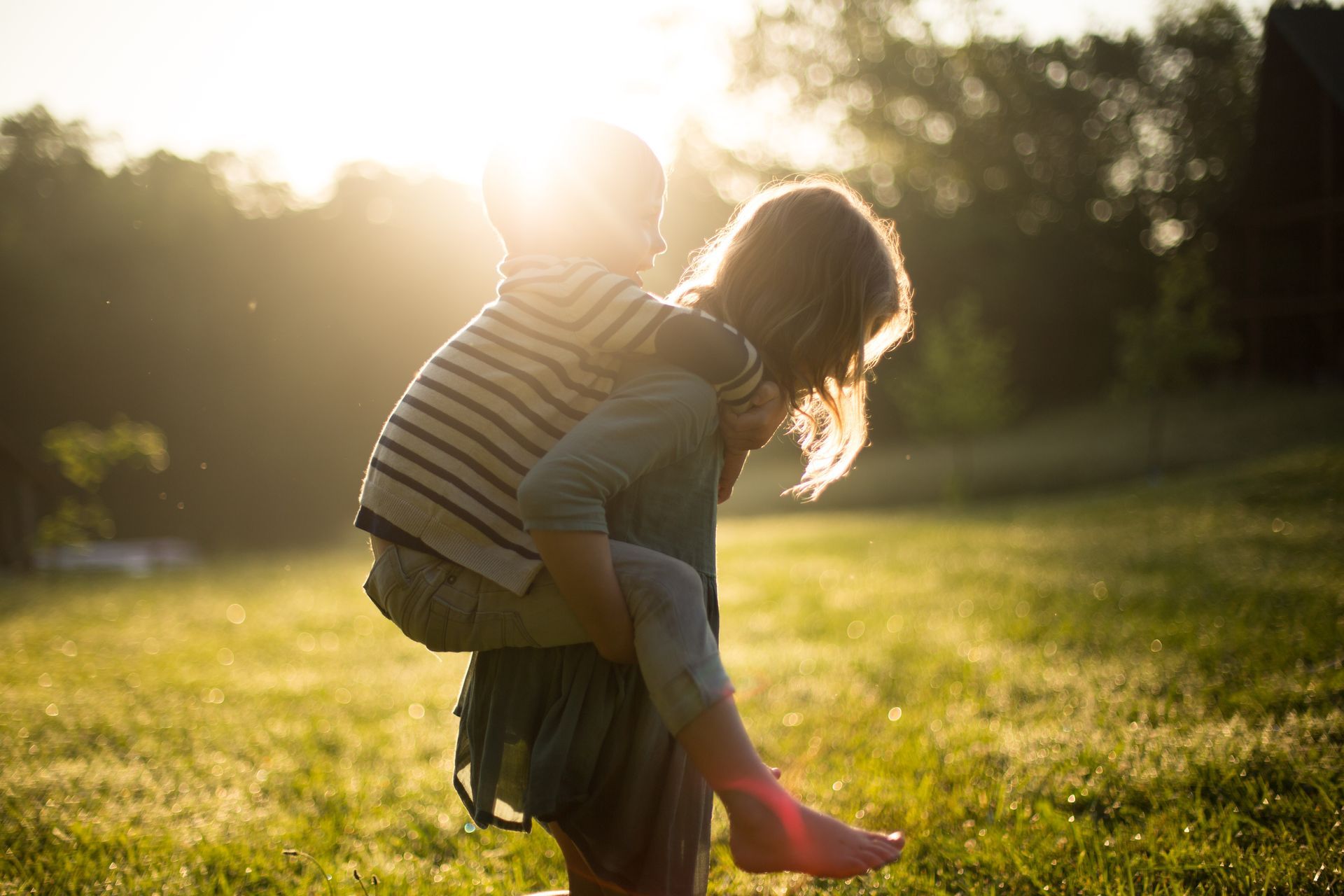 A woman is carrying a child on her back in a field.