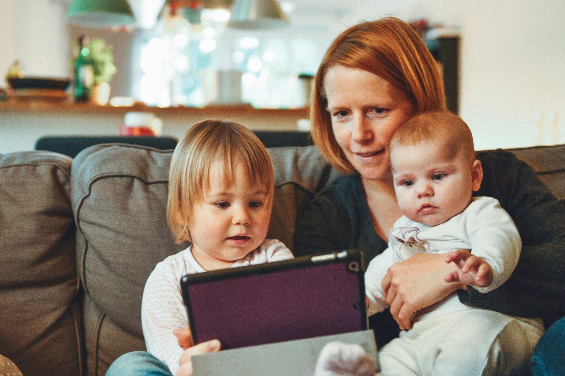 A woman and two children are sitting on a couch looking at a tablet.