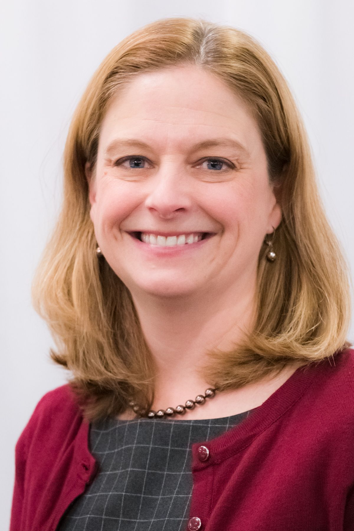 A woman wearing a red cardigan and a necklace is smiling for the camera.