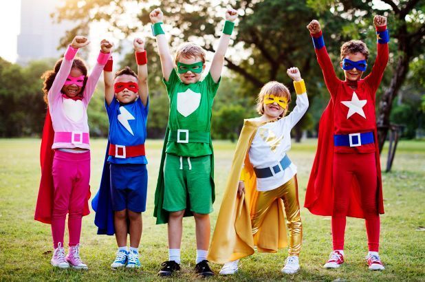 A group of children dressed in superhero costumes are standing in a park.