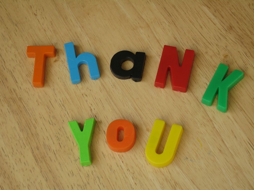 The word thank you is written in colorful letters on a wooden surface
